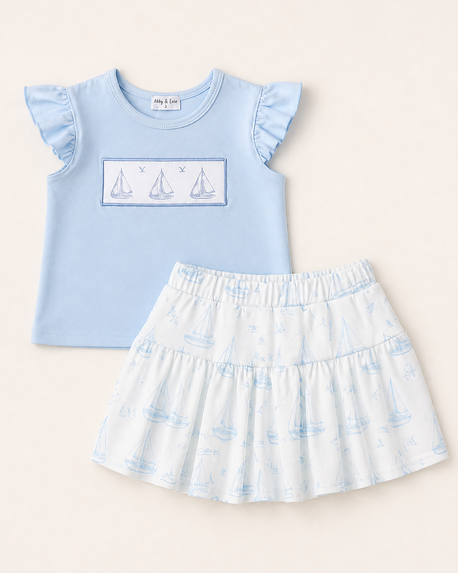 Blue kids ruffle top with embroidered sailboats and white sailboat print skort, front product view