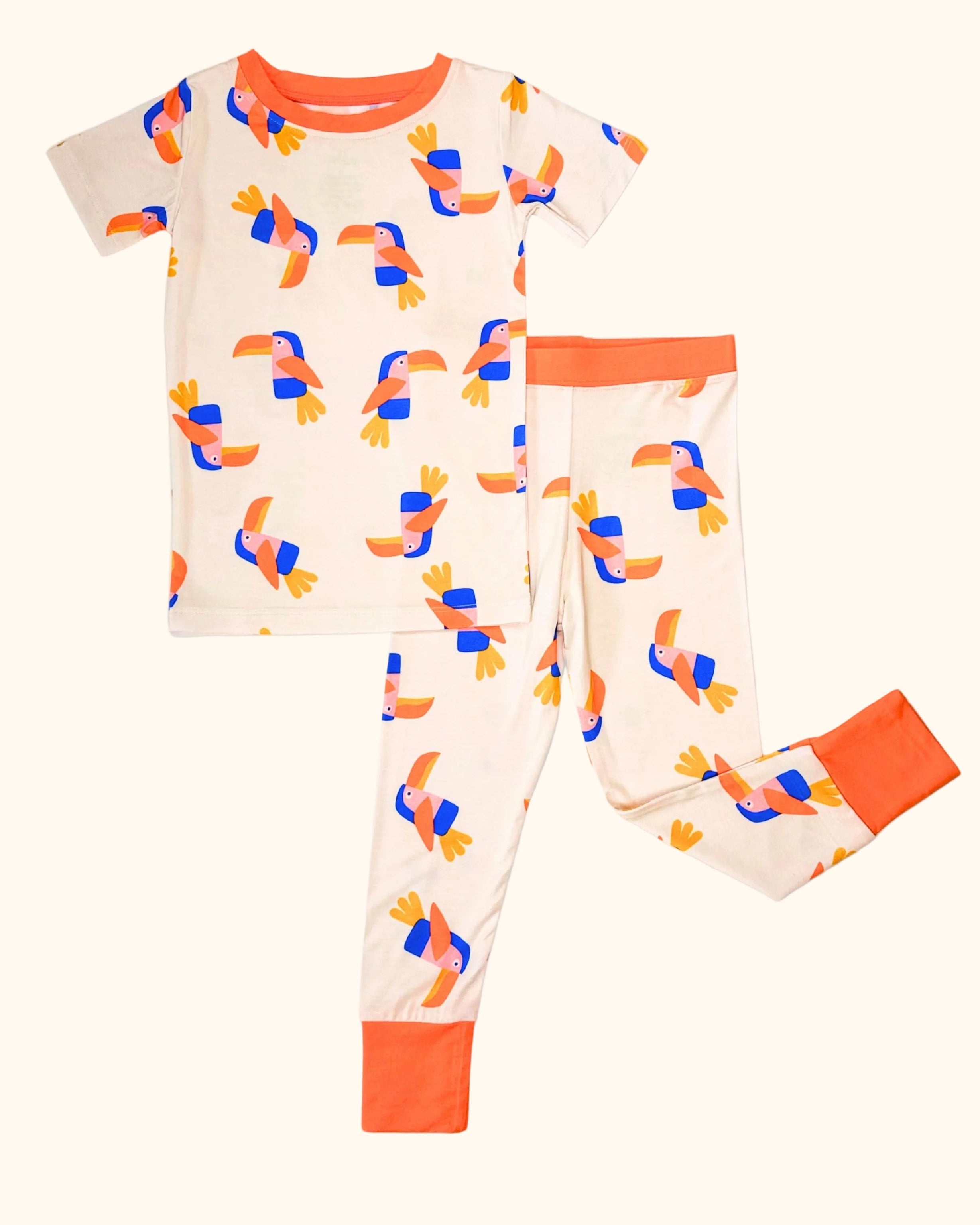Cream kids toucan bamboo pajama set with colorful bird print and orange trim, front flat-lay view