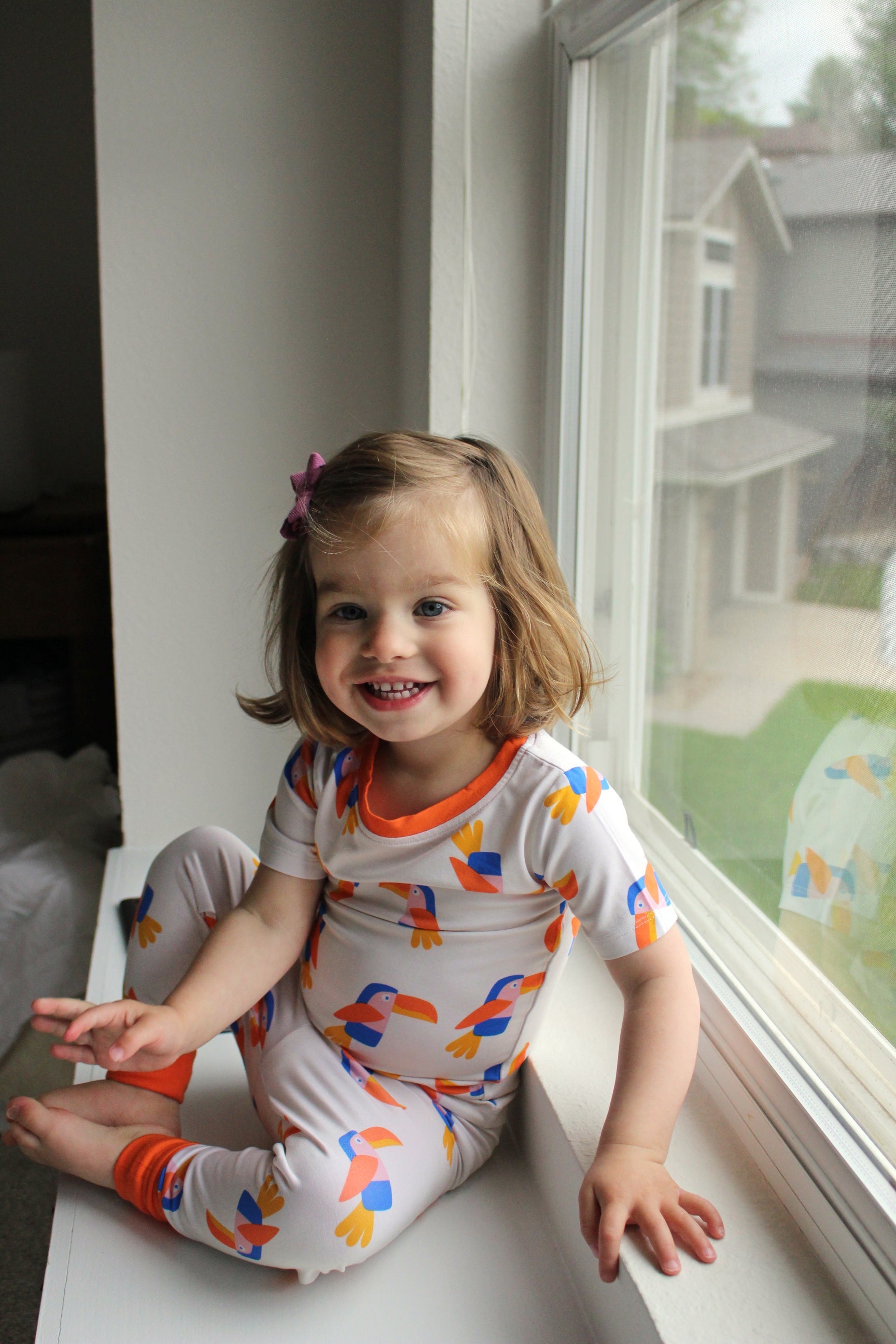 Cream toddler toucan bamboo pajama set with orange neckline and ankle cuffs, modeled front view
