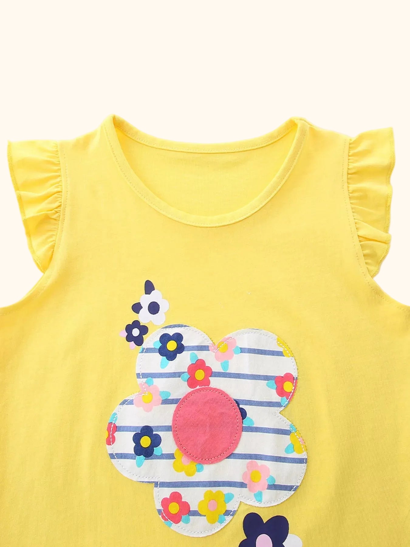 Yellow kids ruffle sleeve top with large striped floral appliqué, upper front close-up