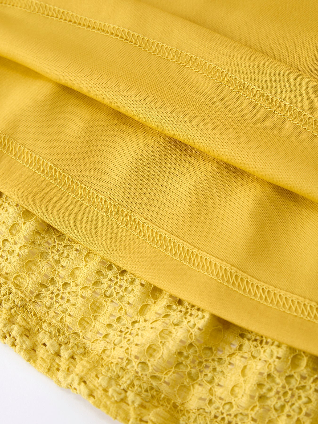 Yellow kids lace dress with smooth inner lining beneath openwork lace, hem detail view