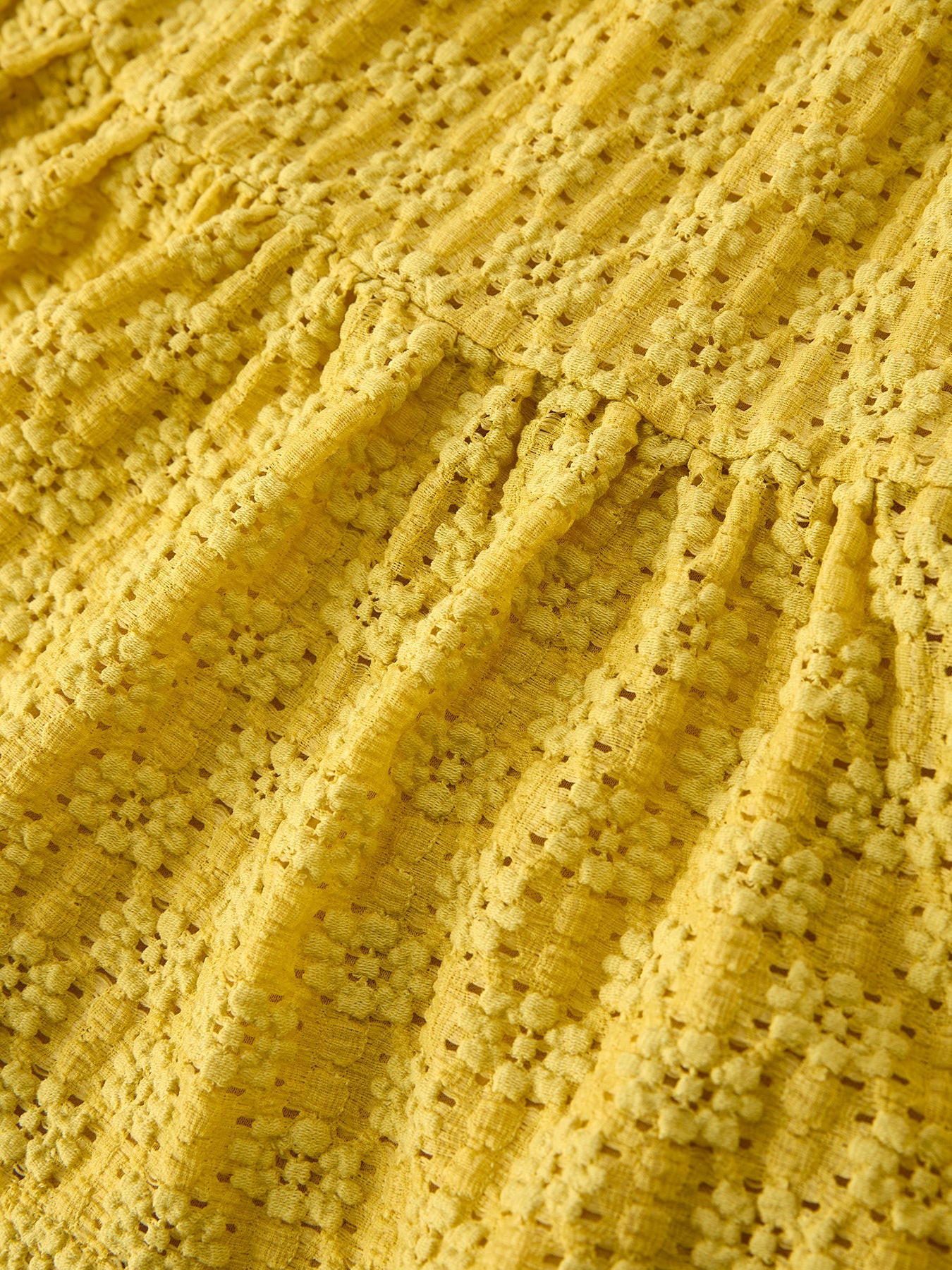 Yellow kids lace tiered dress with gathered waist and textured openwork fabric, seam close-up
