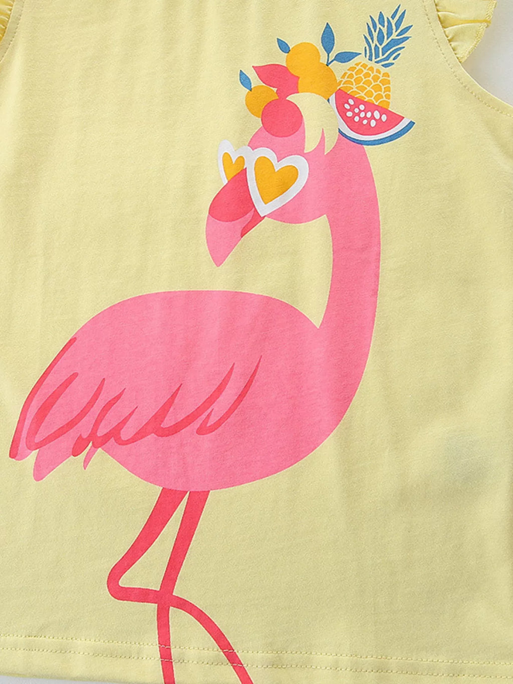 Yellow kids top with pink flamingo, heart sunglasses, and tropical fruit graphic, close-up view