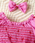 Hot pink baby floral romper dress with smocked bodice, ruffle neckline, and bow headband, close-up view