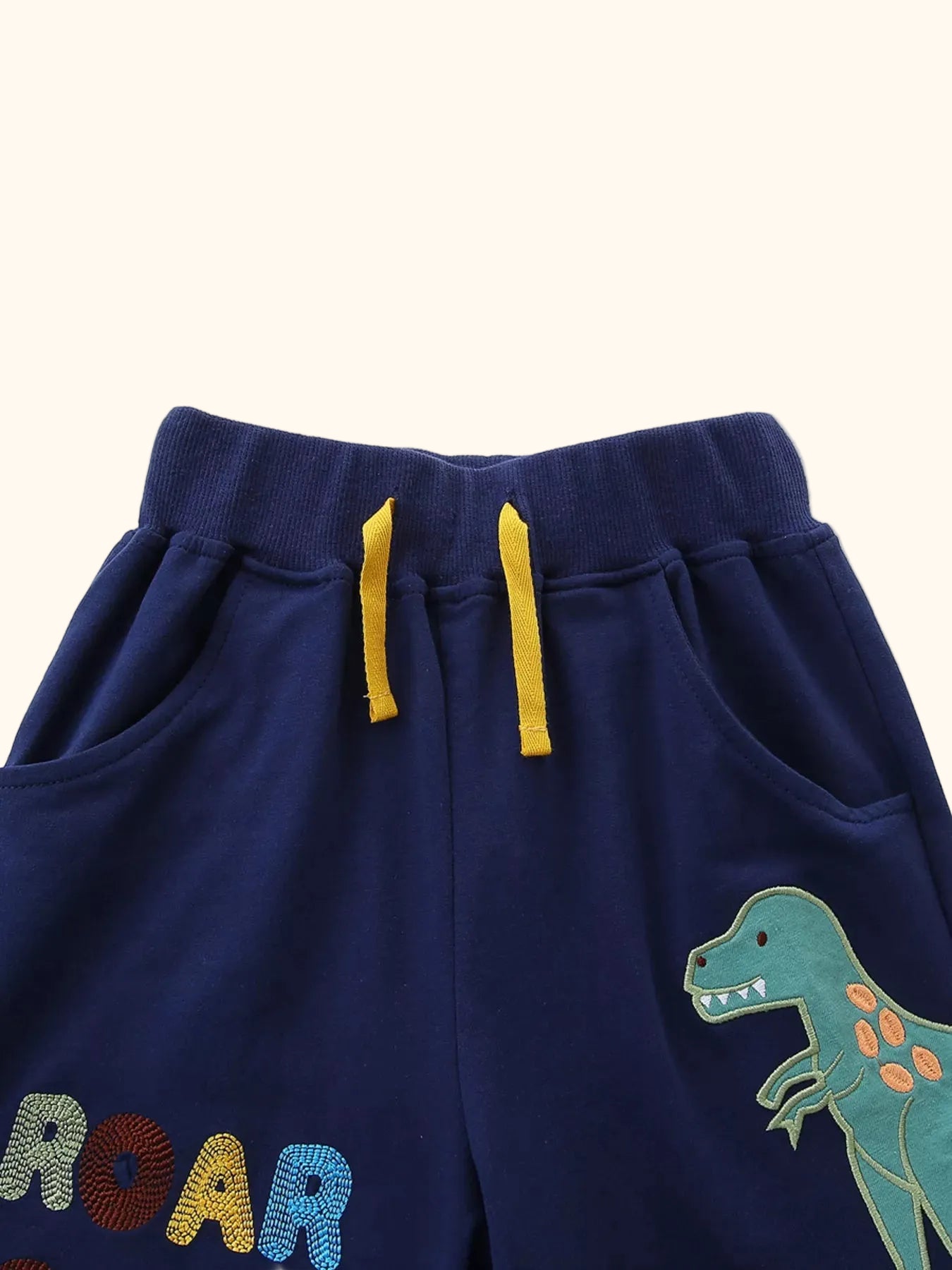 Navy kids shorts with dinosaur graphic, ROAR-SOME lettering, pockets and yellow drawcord, front detail